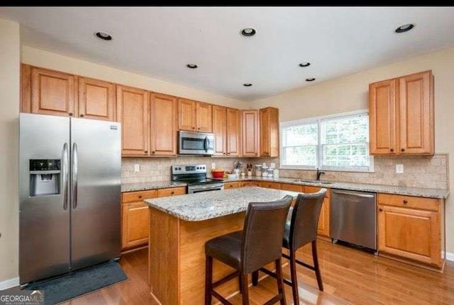 kitchen with a breakfast bar area, light stone counters, wood-type flooring, a center island, and appliances with stainless steel finishes