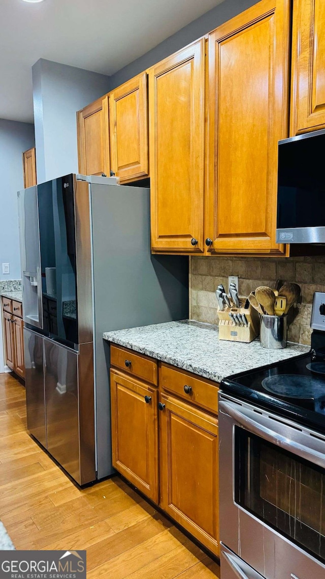 kitchen with stainless steel appliances, light stone countertops, decorative backsplash, and light hardwood / wood-style flooring