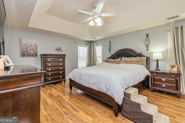 bedroom featuring light hardwood / wood-style flooring, ceiling fan, and a tray ceiling