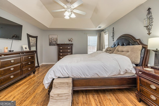 bedroom with light hardwood / wood-style flooring, ceiling fan, and a tray ceiling