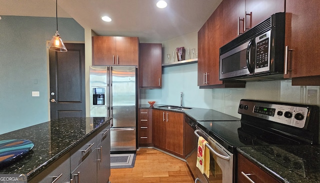 kitchen featuring sink, dark stone countertops, hanging light fixtures, stainless steel appliances, and light wood-type flooring