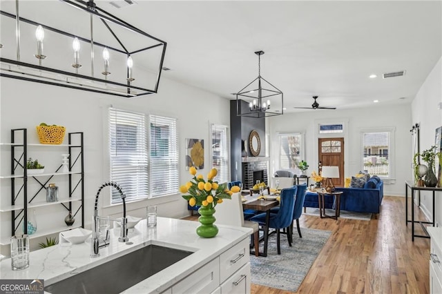 kitchen with pendant lighting, sink, white cabinetry, a fireplace, and light wood-type flooring