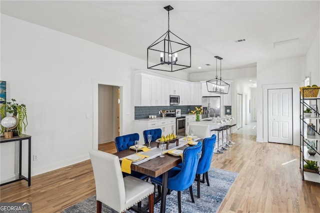 dining space featuring sink, a notable chandelier, and light hardwood / wood-style flooring