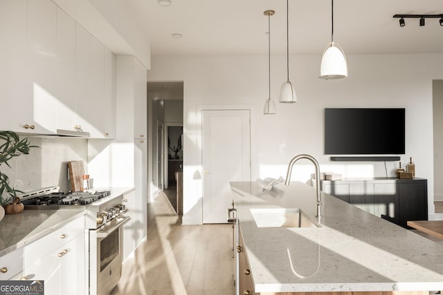 kitchen with high end stove, a sink, white cabinetry, light wood finished floors, and a center island with sink