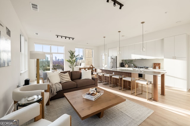 living room with rail lighting, visible vents, light wood finished floors, and a view of city