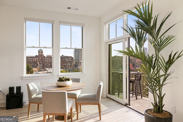 dining room with baseboards, light wood-style flooring, visible vents, and a city view