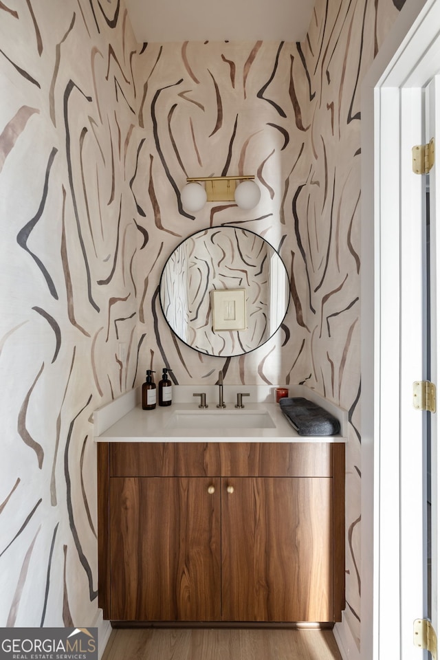 bathroom with wallpapered walls, wood finished floors, and vanity