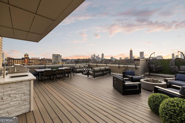wooden terrace with a view of city, an outdoor living space with a fire pit, an outdoor kitchen, and area for grilling