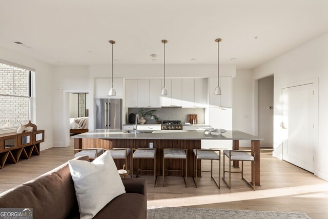 kitchen featuring tasteful backsplash, stove, high end fridge, white cabinetry, and a sink