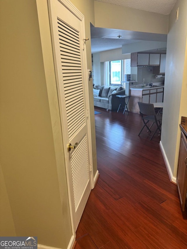 hall featuring a textured ceiling, dark wood finished floors, and baseboards