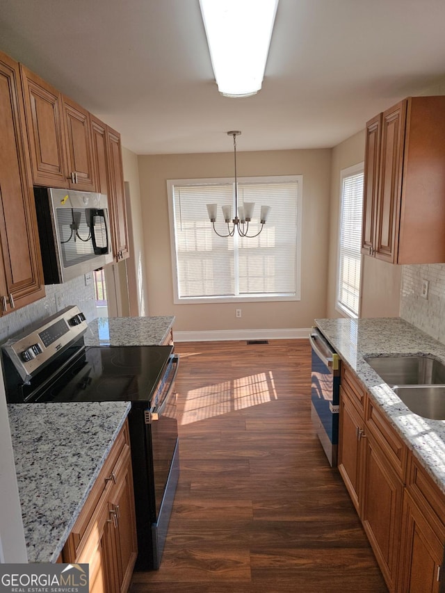 kitchen with light stone counters, hanging light fixtures, dark hardwood / wood-style floors, stainless steel appliances, and decorative backsplash