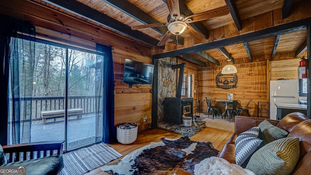 living room with light hardwood / wood-style flooring, wood walls, a wood stove, wooden ceiling, and beam ceiling