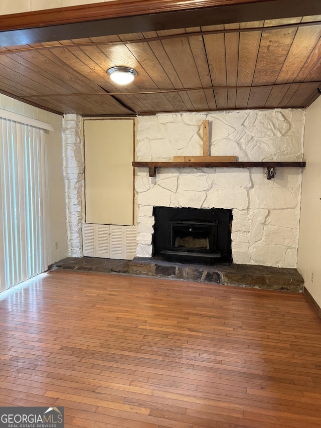 unfurnished living room featuring hardwood / wood-style floors, a stone fireplace, and wooden ceiling