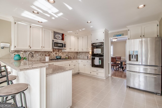 kitchen featuring kitchen peninsula, stainless steel appliances, ornamental molding, white cabinets, and a kitchen bar