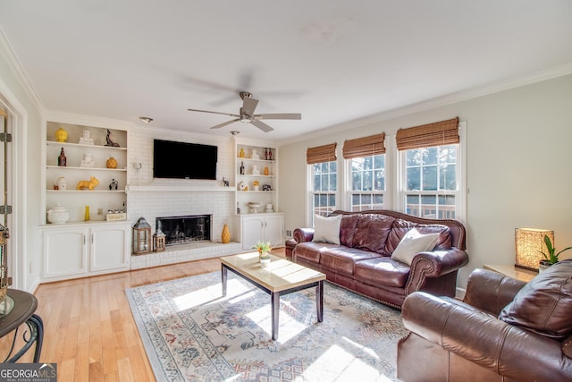 living room with a brick fireplace, built in shelves, light hardwood / wood-style floors, crown molding, and ceiling fan