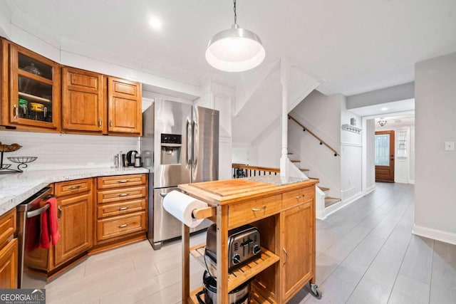 kitchen featuring light stone counters, decorative light fixtures, stainless steel appliances, brown cabinetry, and glass insert cabinets