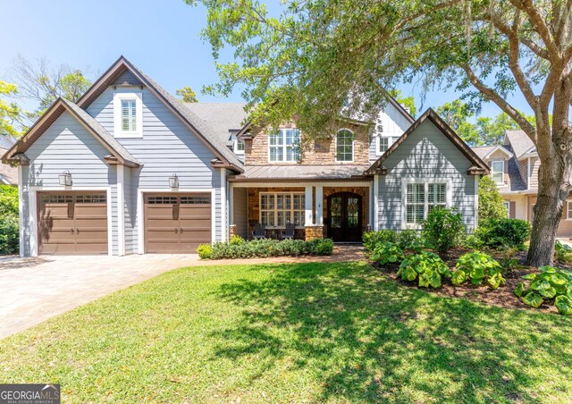 craftsman house with a garage, stone siding, a front lawn, french doors, and driveway