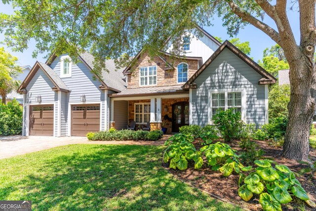 view of front of property featuring driveway, stone siding, a front lawn, and covered porch