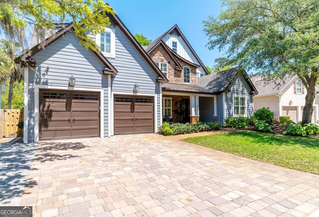 craftsman inspired home with a front yard, stone siding, and decorative driveway