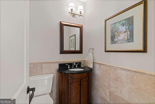 bathroom featuring toilet, tile walls, vanity, and a wainscoted wall