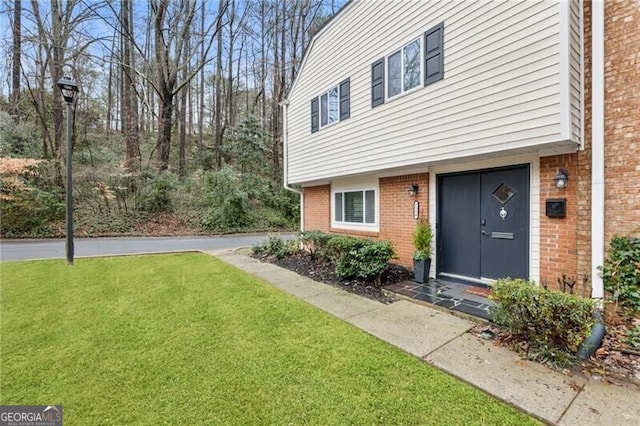 doorway to property with brick siding and a yard