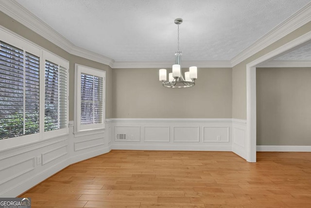 unfurnished dining area featuring ornamental molding, light wood finished floors, visible vents, and a notable chandelier