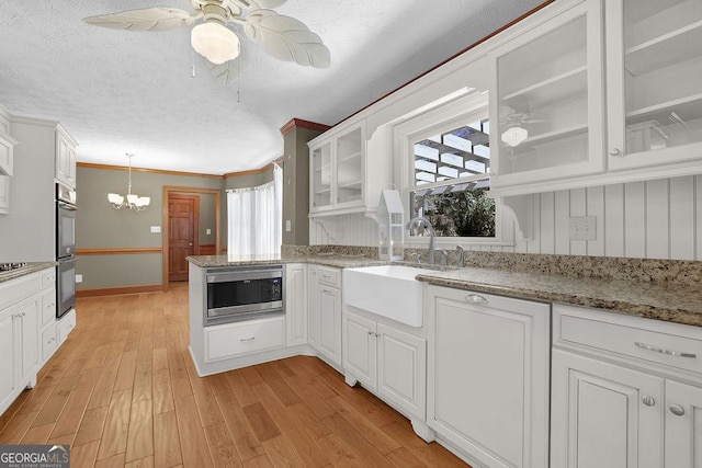 kitchen with light wood finished floors, appliances with stainless steel finishes, a sink, and white cabinetry