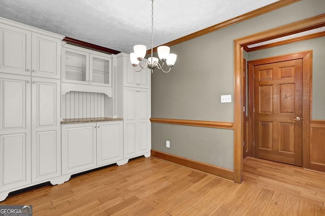 unfurnished dining area with an inviting chandelier, baseboards, ornamental molding, and light wood-style floors