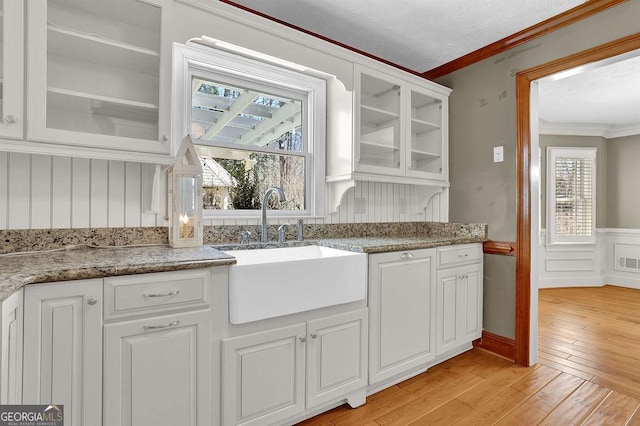 kitchen with light wood-style flooring, ornamental molding, glass insert cabinets, white cabinets, and a sink