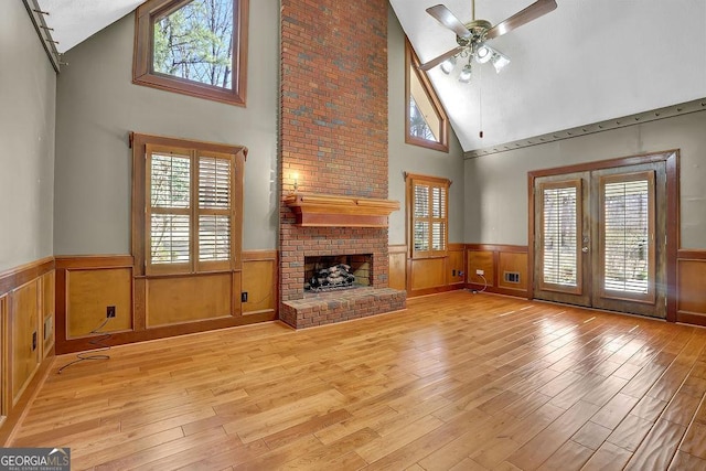 unfurnished living room featuring a brick fireplace, wainscoting, plenty of natural light, and wood finished floors