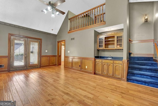 unfurnished living room with a wainscoted wall, stairway, light wood-type flooring, and a sink