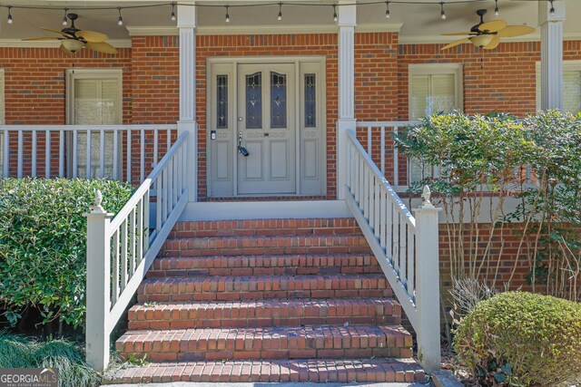 view of exterior entry featuring covered porch, ceiling fan, and brick siding