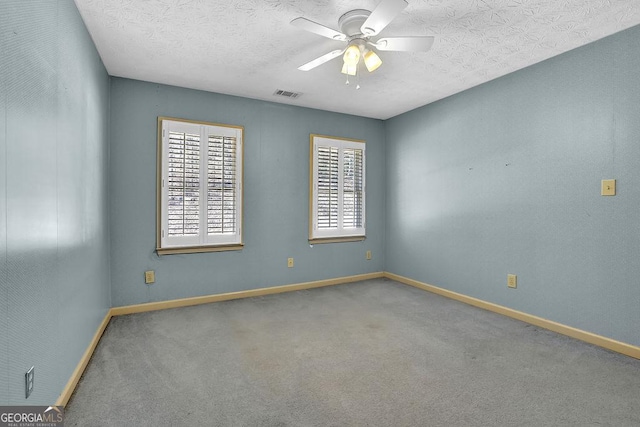 carpeted empty room featuring a ceiling fan, visible vents, a textured ceiling, and baseboards