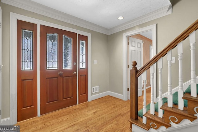 entryway with visible vents, baseboards, light wood-style flooring, ornamental molding, and stairs