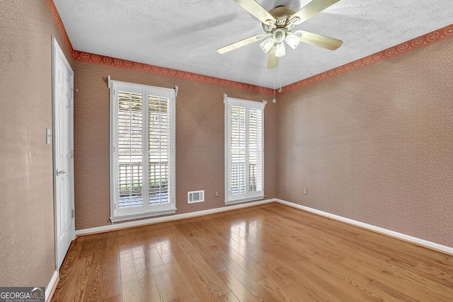 empty room featuring a wealth of natural light, hardwood / wood-style flooring, visible vents, and wallpapered walls