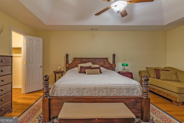 bedroom with ceiling fan, a tray ceiling, and light hardwood / wood-style floors