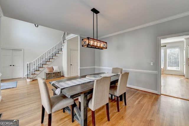 dining space featuring ornamental molding, light wood-type flooring, baseboards, and stairs