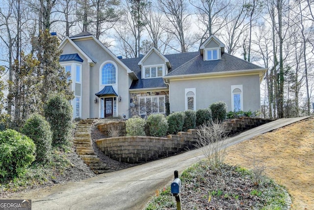 traditional-style house featuring roof with shingles and stucco siding