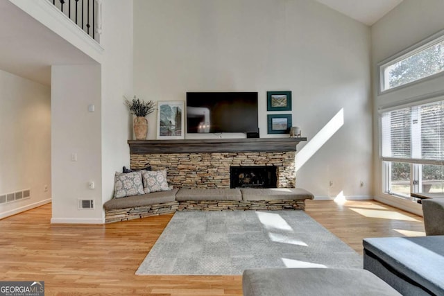 living area with light wood finished floors, a high ceiling, visible vents, and a stone fireplace