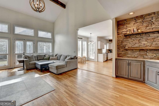 living area featuring high vaulted ceiling, french doors, light wood-type flooring, beamed ceiling, and an inviting chandelier