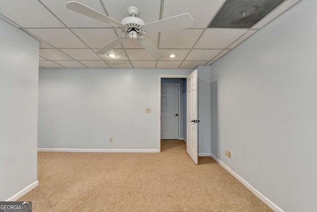 empty room with baseboards, a drop ceiling, a ceiling fan, and light colored carpet