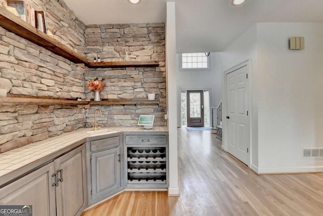 bar featuring baseboards, visible vents, indoor wet bar, light wood-style floors, and a sink