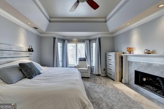 bedroom with a raised ceiling, light colored carpet, visible vents, a tiled fireplace, and ornamental molding