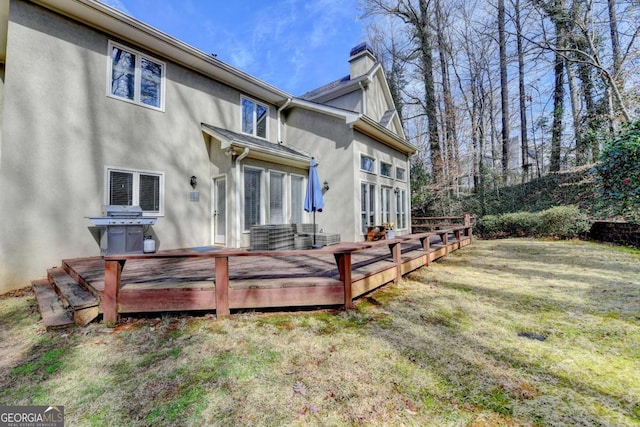 rear view of property with a chimney, a yard, a deck, and stucco siding