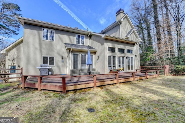 back of property with a lawn, a chimney, fence, a wooden deck, and stucco siding