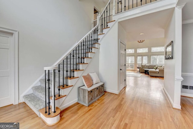 stairway with visible vents, wood finished floors, a towering ceiling, and baseboards