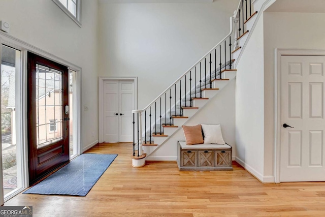 foyer entrance with stairs, light wood finished floors, a towering ceiling, and baseboards