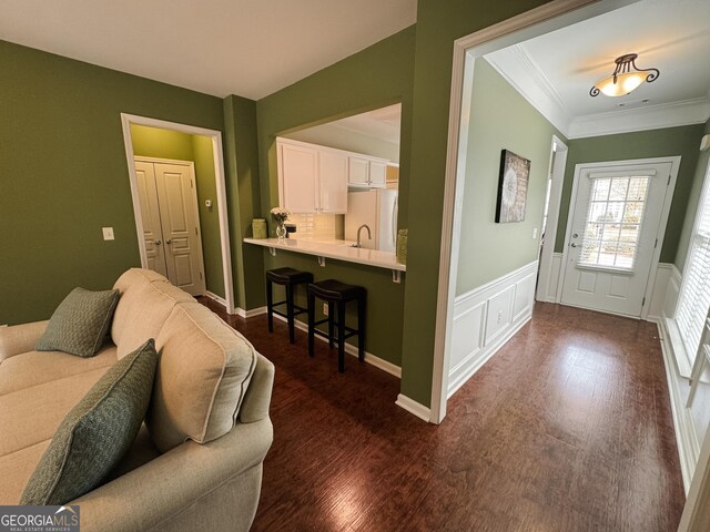 living area featuring a decorative wall, wainscoting, dark wood finished floors, and crown molding