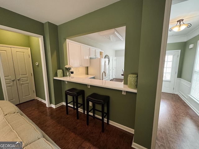 kitchen featuring dark wood-type flooring, a breakfast bar, white cabinetry, light countertops, and freestanding refrigerator