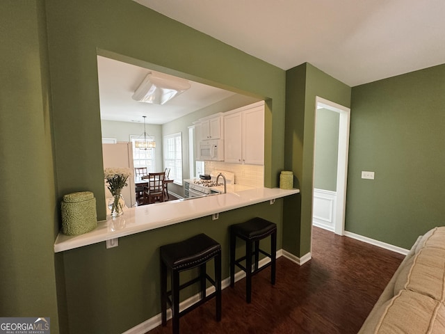 kitchen with white appliances, dark wood-style flooring, a breakfast bar, white cabinets, and decorative backsplash